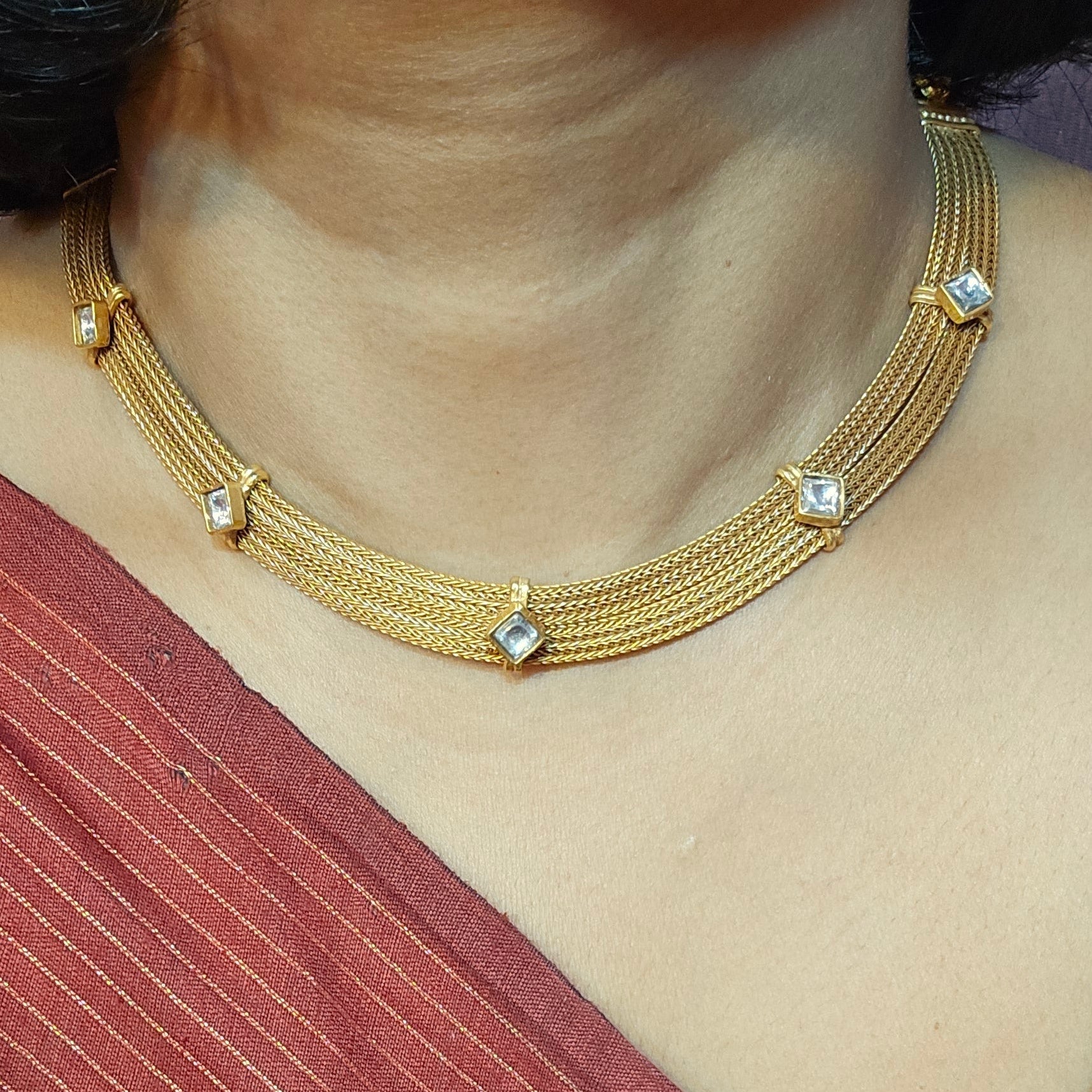 Gold necklace with diamond-like stones worn by a person in a red and blue outfit.