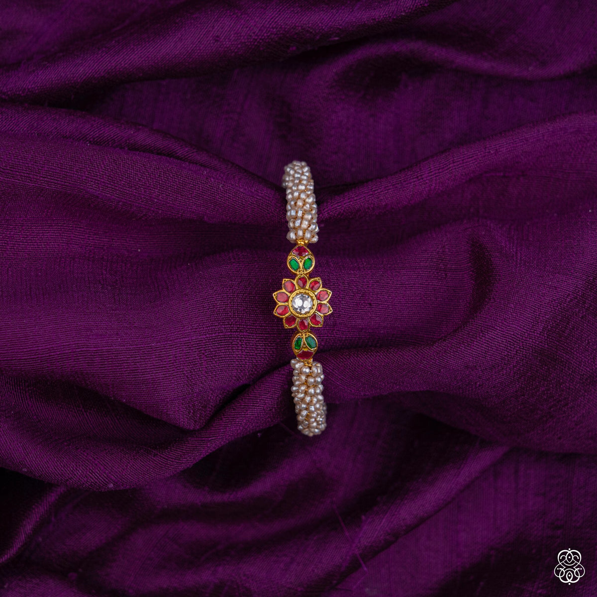 Close view of the ruby, emerald and kundan flower on the Muktakusuma pearl bangle